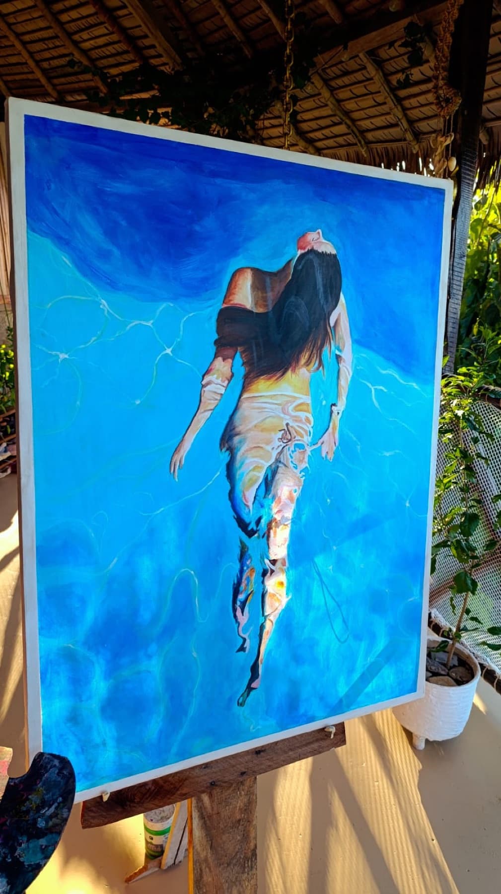 Peinture d'une femme flottant sur le ventre dans une eau turquoise, vue du dessus, ses longs cheveux noirs déployés autour d'elle et les reflets du soleil dessinant des lignes claires à la surface.