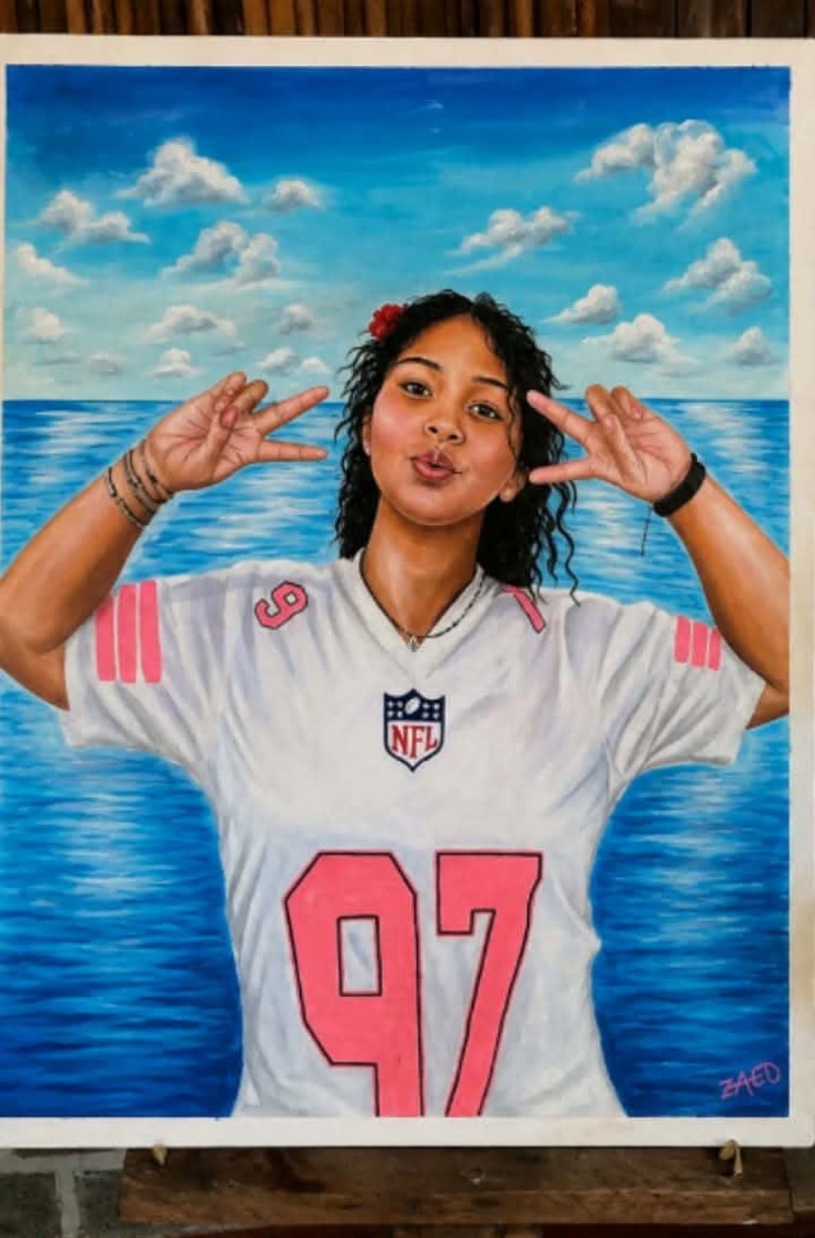 Portrait peint d'une jeune femme aux cheveux bouclés faisant un signe des deux mains, vêtue d'un maillot de sport blanc et rose numéro 97, devant la mer et un ciel parsemé de nuages.
